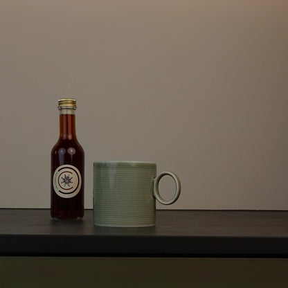 Chai Connection (Geschenk-) Flasche mit Chai-Sirup – Chai Konzentrat neben grüner Tasse, produziert in der Schweiz für Chai Lattes, Cocktails und viele kreative Rezepte. 
